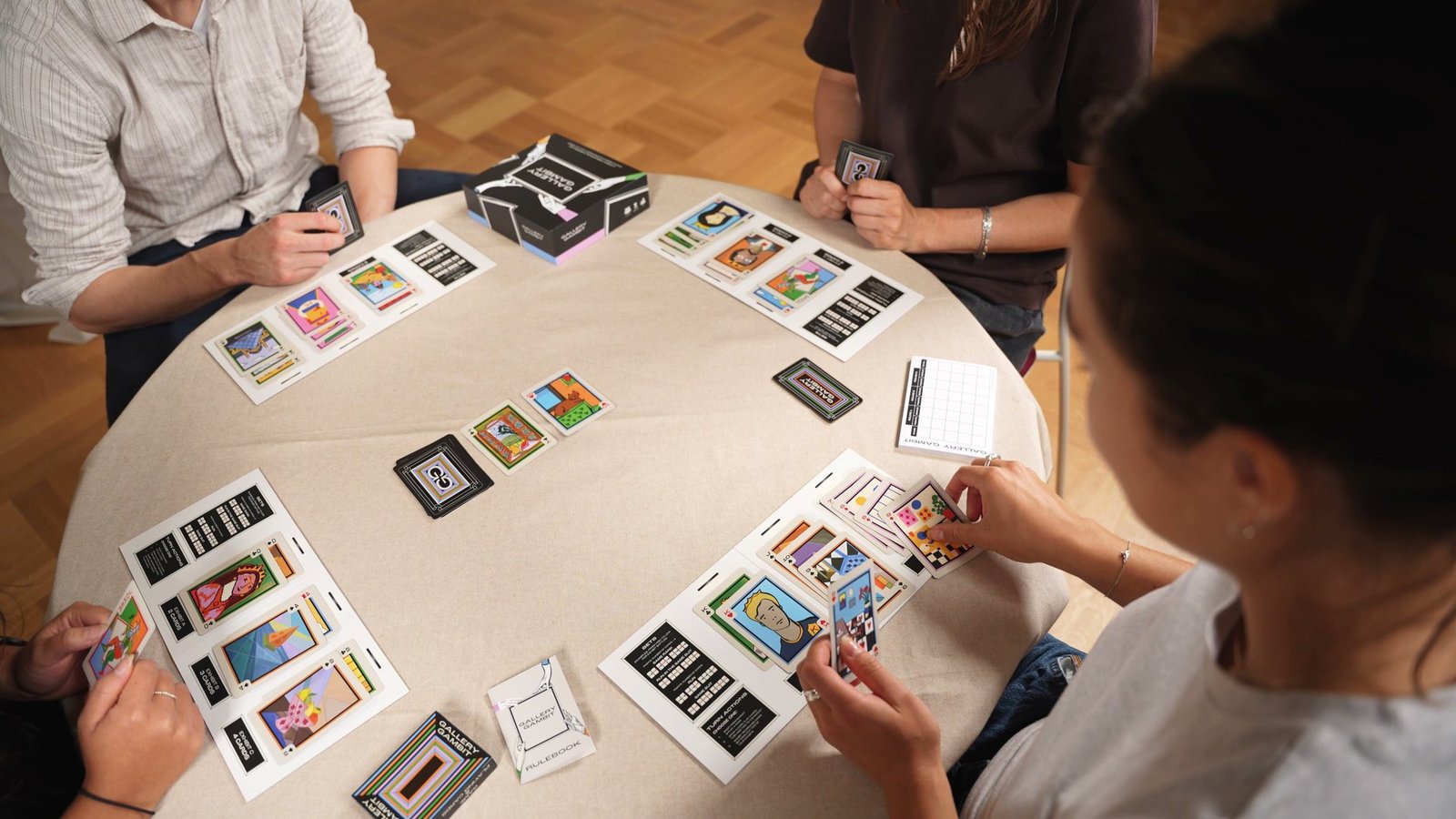 Players lean over a table and pick painted cards from the shared Market.