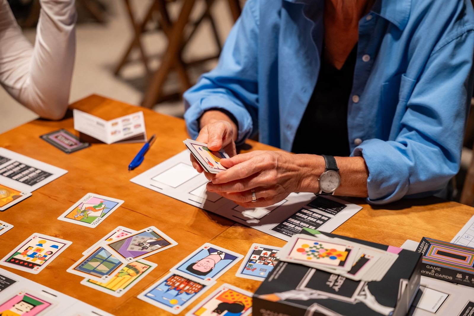 Close view of hands holding a fan of Gallery Gambit cards above the player boards.