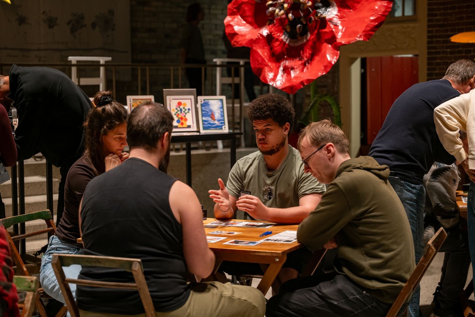 Four players mid-game at a wooden table, with the card display behind them.